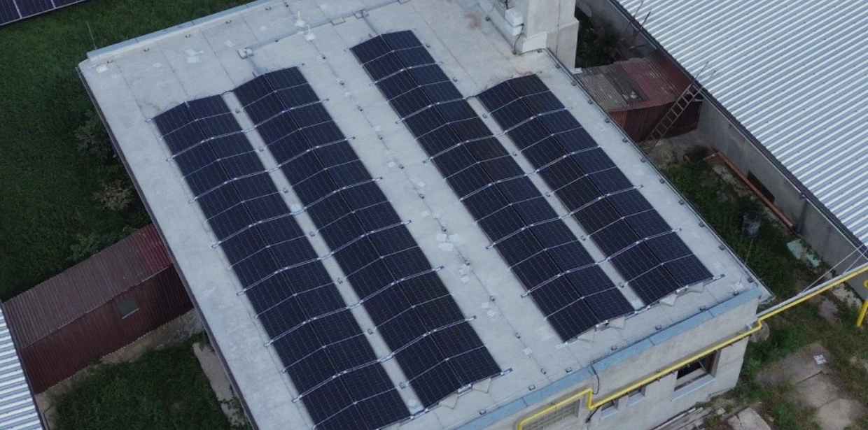 An aerial view of an industrial flat rooftop featuring four long rows of black solar panels installed for renewable energy.